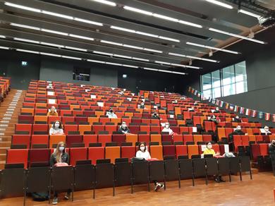 Begrüßung der Austauschstudierenden in Zeiten der Pandemie: m großen Hörsaal der Hochschule Düsseldorf mit 400 Plätzen sitzen 22 Austauschstudierende mit Sicherheitsabstand verstreut auf den roten Sitzen. Alle tragen eine Maske.